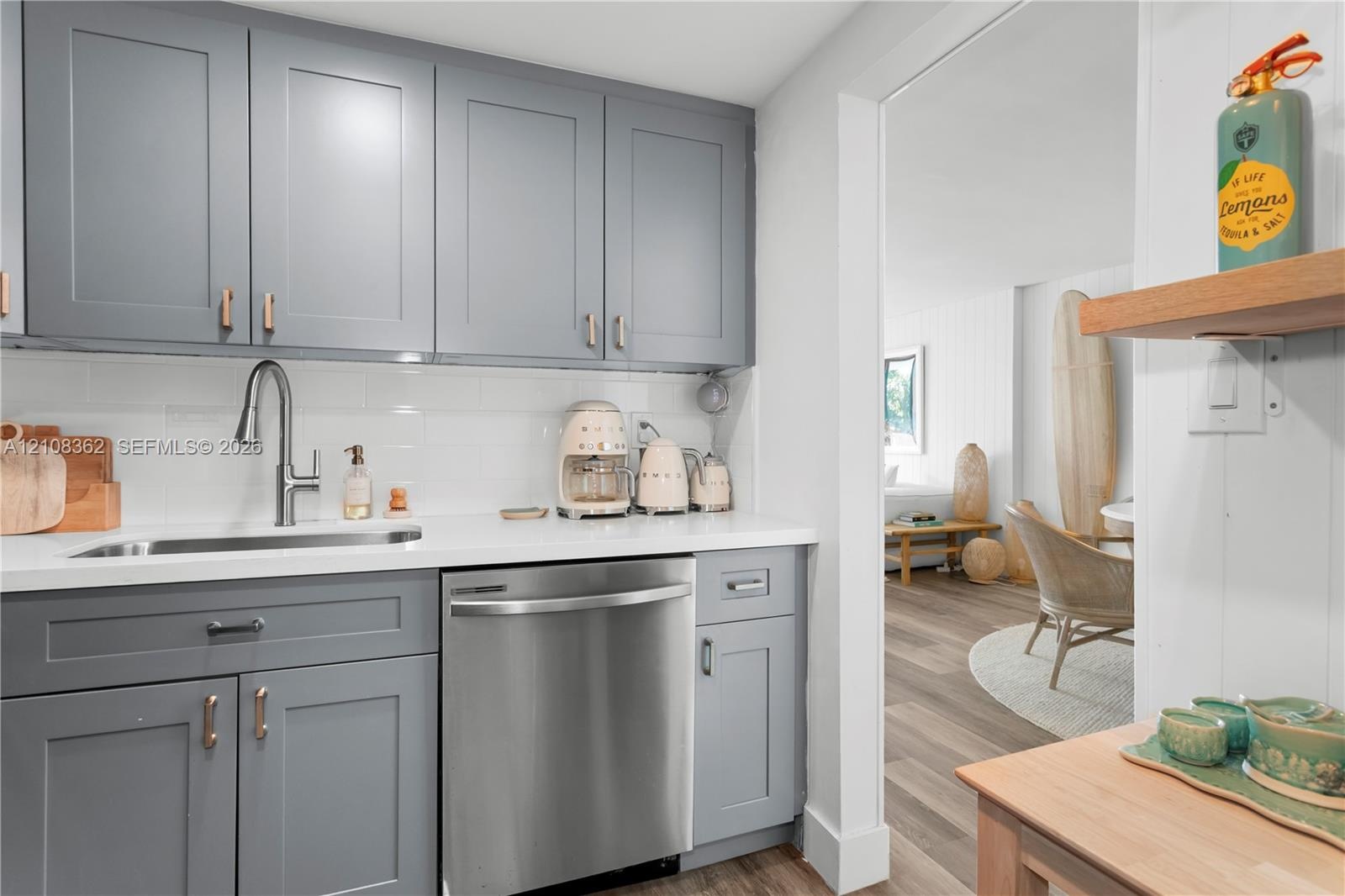 Kitchen featuring grey shaker-style cabinetry, white subway tile backsplash, solid-surface countertops, undermount stainless steel sink with pull-down