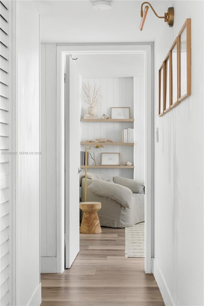 Vertical shiplap wall paneling, light-tone wood-finish flooring, three floating wooden wall shelves, and an adjustable brass-finish wall sconce