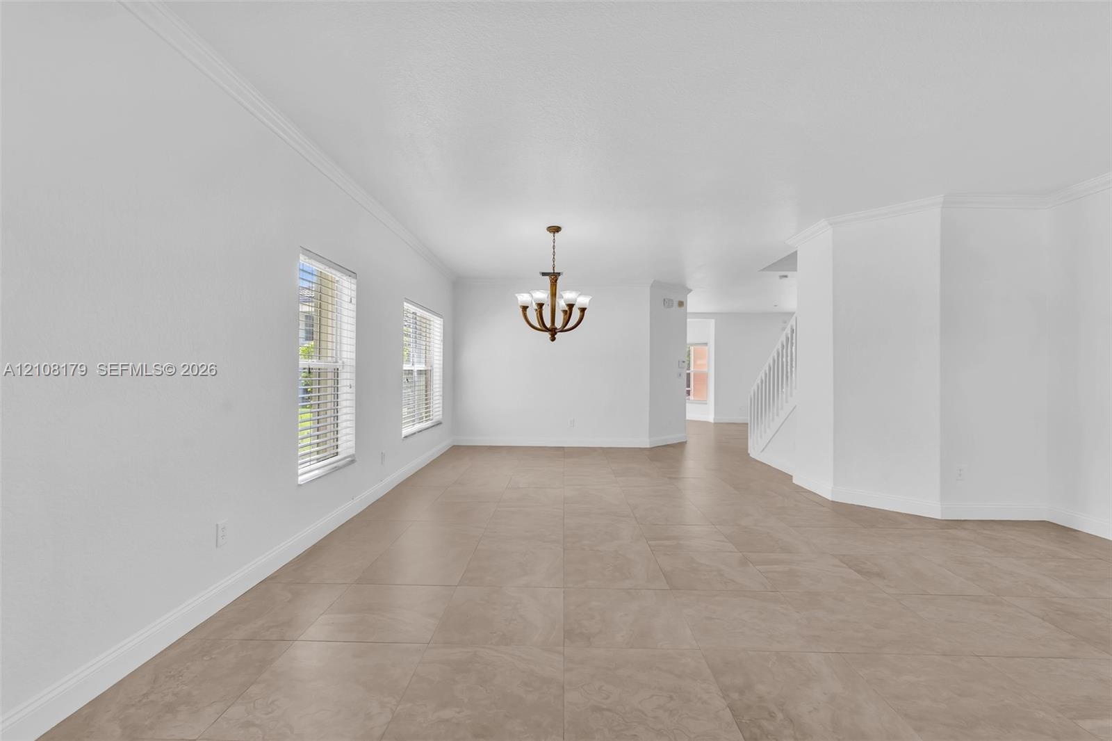 Large-format tile flooring, multi-light chandelier with metallic finish, crown molding, and staircase with white railings