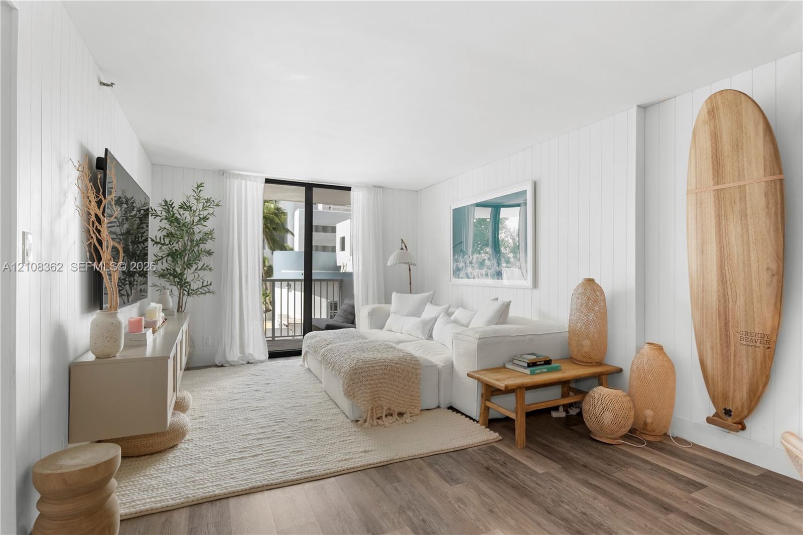 Living area featuring white vertical shiplap wall paneling, wood-finish flooring, and sliding glass doors with balcony access
