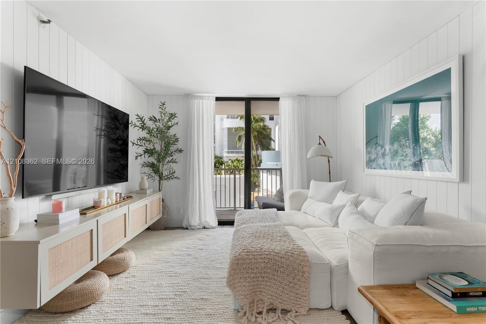Living area featuring vertical plank wall paneling, a wall-mounted built-in console with cane detailing, and glass sliding doors leading to an exterio