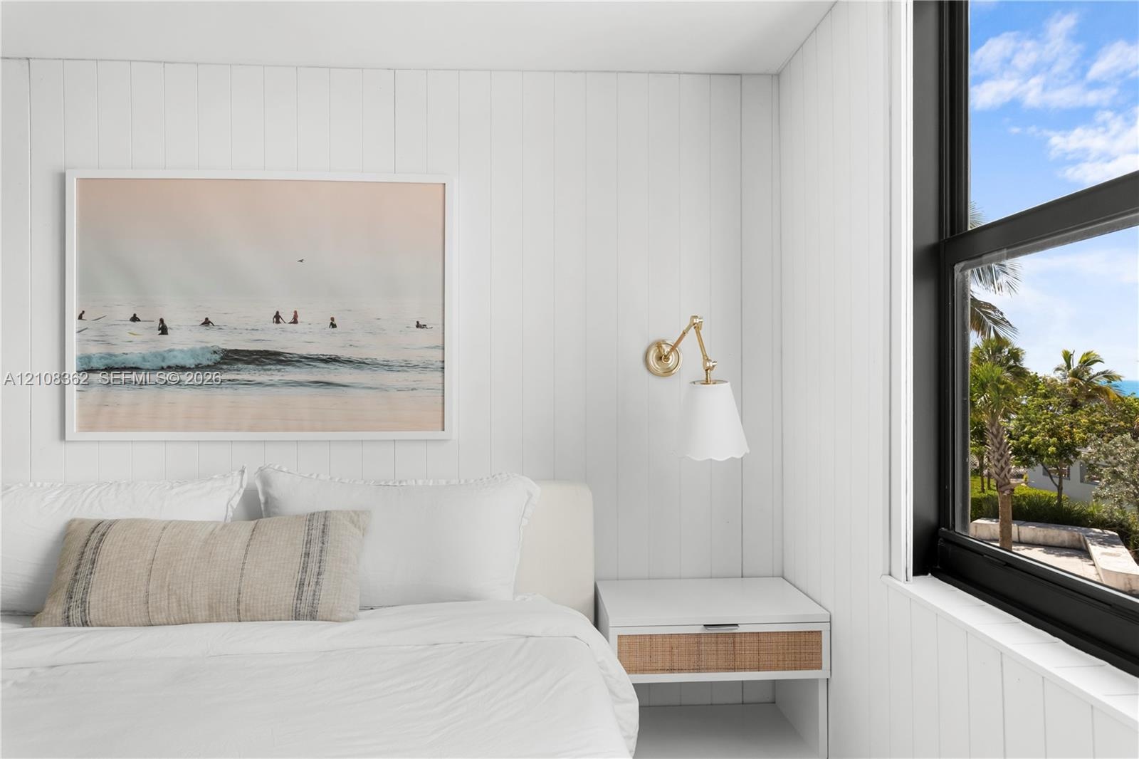 Vertical white shiplap walls, brass-finish swing-arm wall sconce, and black-framed windows with exterior scenery