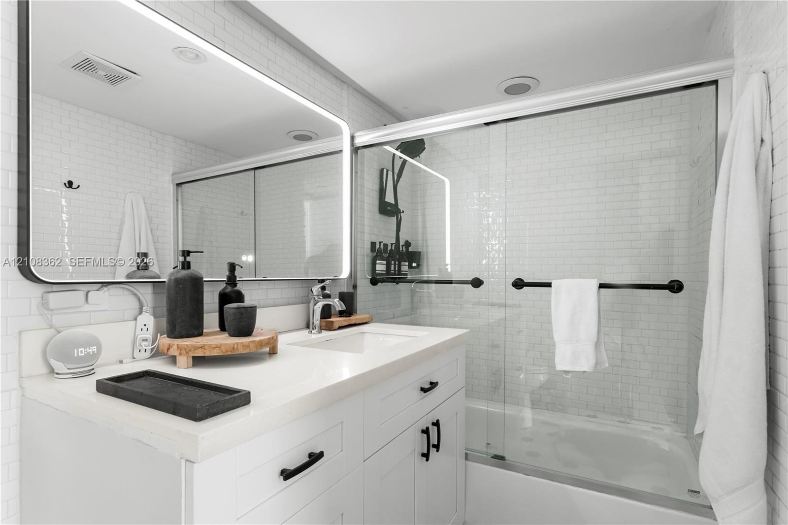 White vanity featuring a solid surface countertop, undermount sink, and matte black hardware, paired with a subway tile shower surround, sliding glass