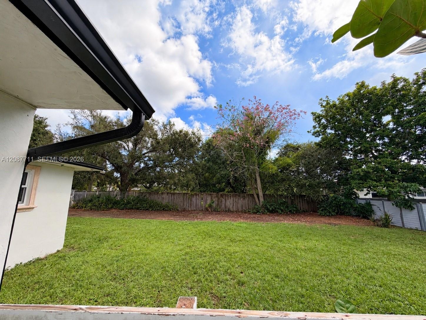 Backyard featuring an expansive lawn, mature tree canopy, and wood fencing