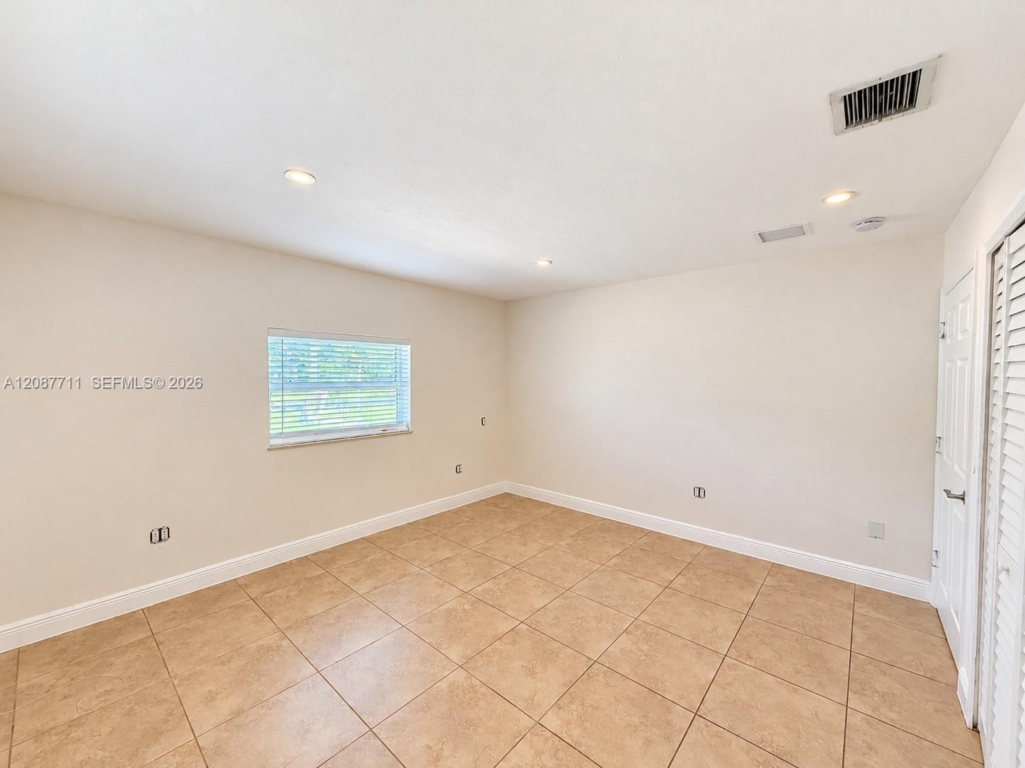 Interior space featuring neutral-toned tile flooring, recessed ceiling lighting, a single window, and a louvered bi-fold closet door