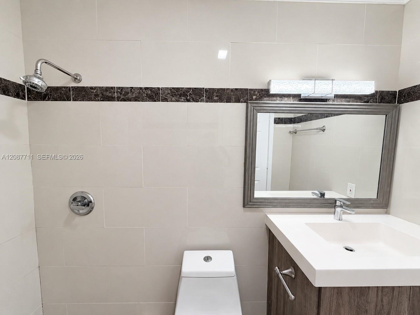 Bathroom featuring floor-to-ceiling cream tiling with dark stone accent banding, a vanity with an integrated basin, wall-mounted brushed-metal hardwar
