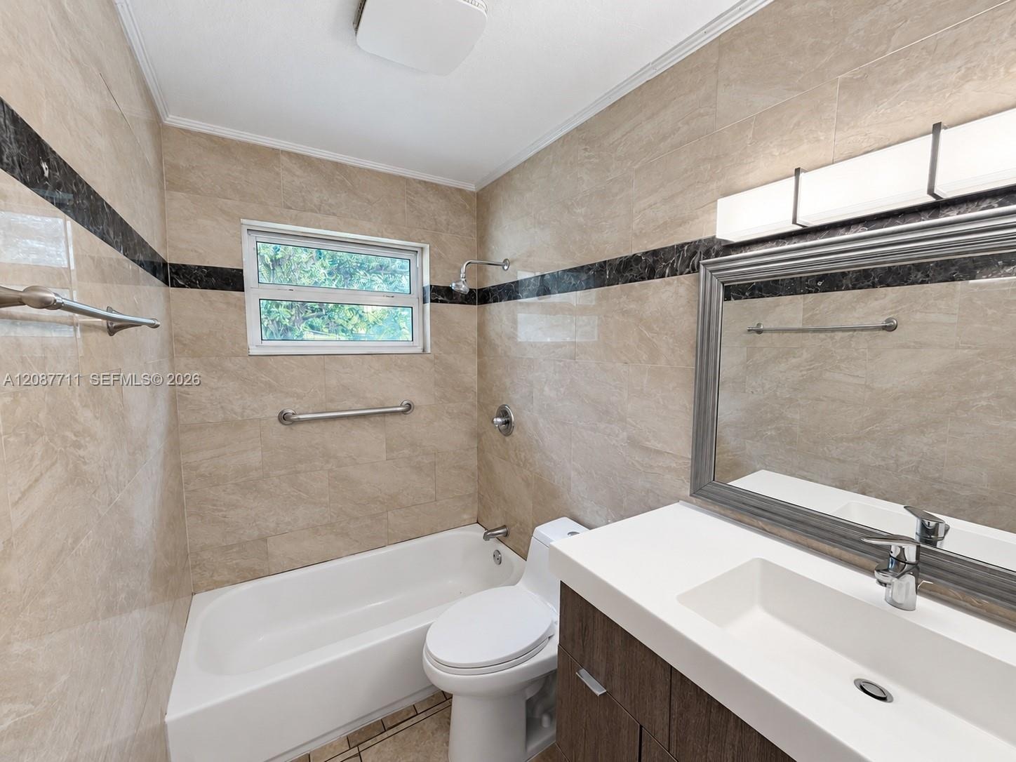 Full-height neutral stone tiling with decorative dark stone accent banding, modern wood-finish vanity with integrated rectangular sink, wall-mounted m