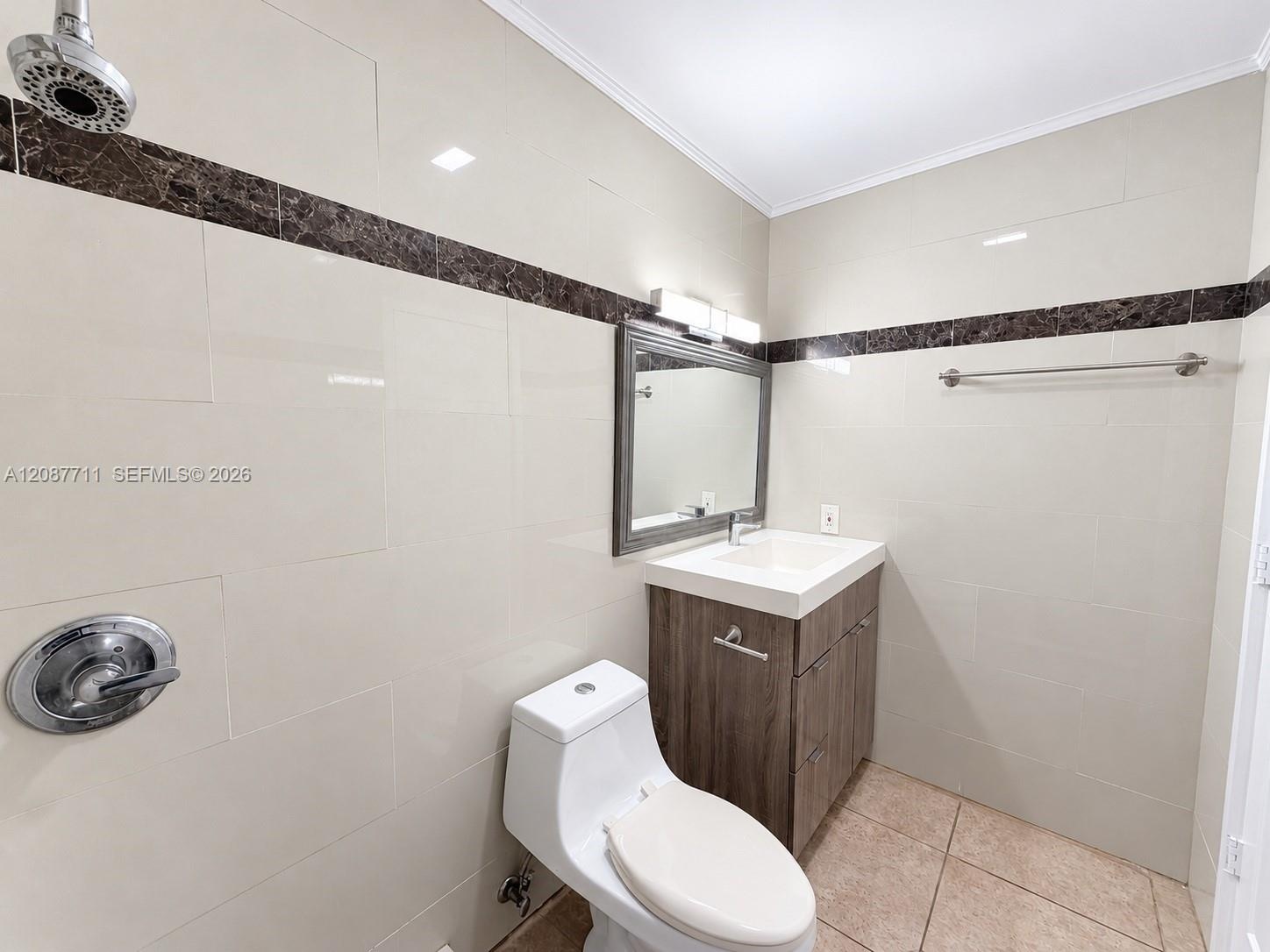 Bathroom featuring light-toned wall tile with dark stone accent trim, wood-finish vanity with a rectangular sink, wall-mounted light fixture, and meta