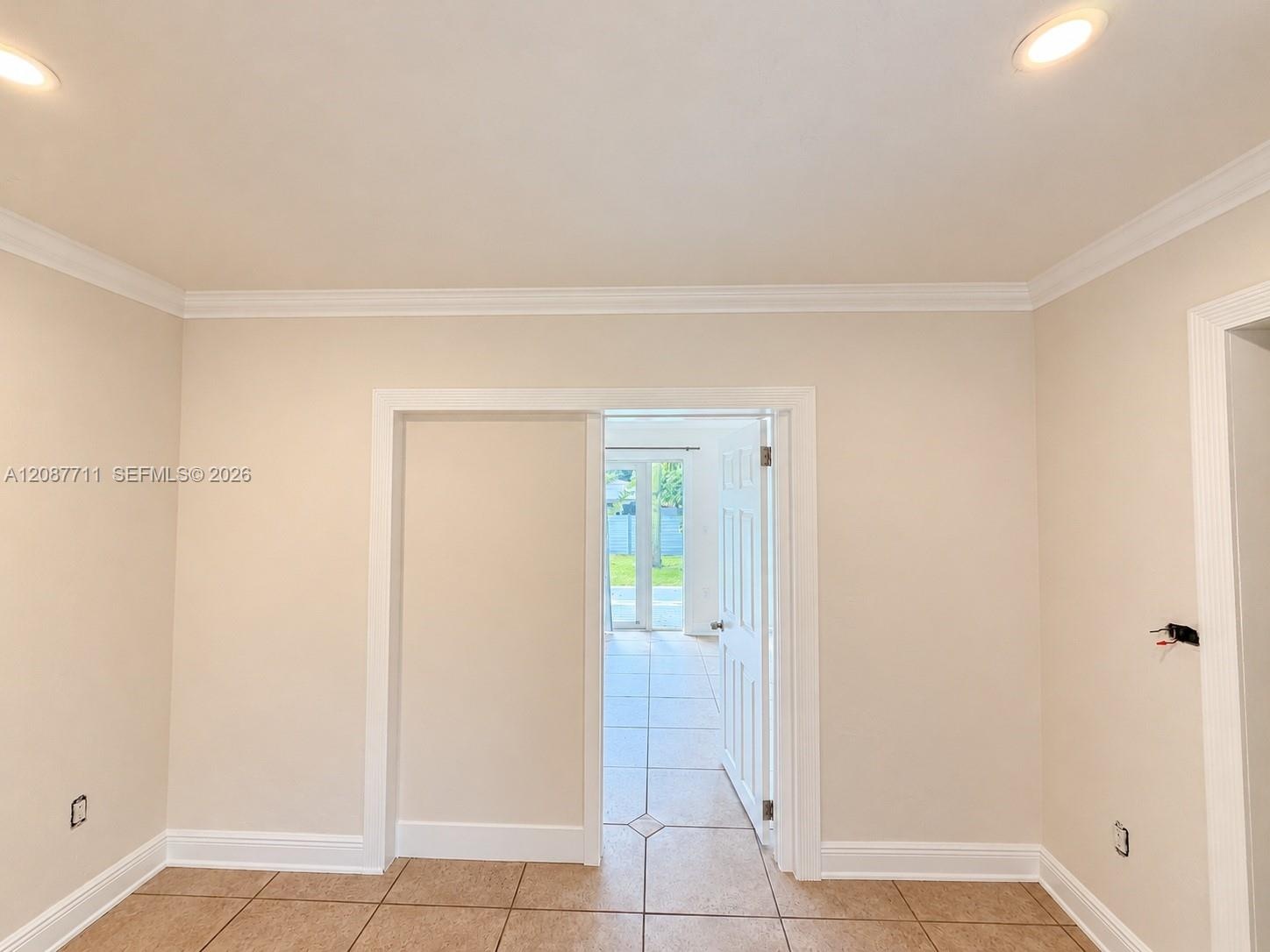 Neutral-toned interior space featuring crown molding, recessed lighting, and tile flooring with decorative inlay accents