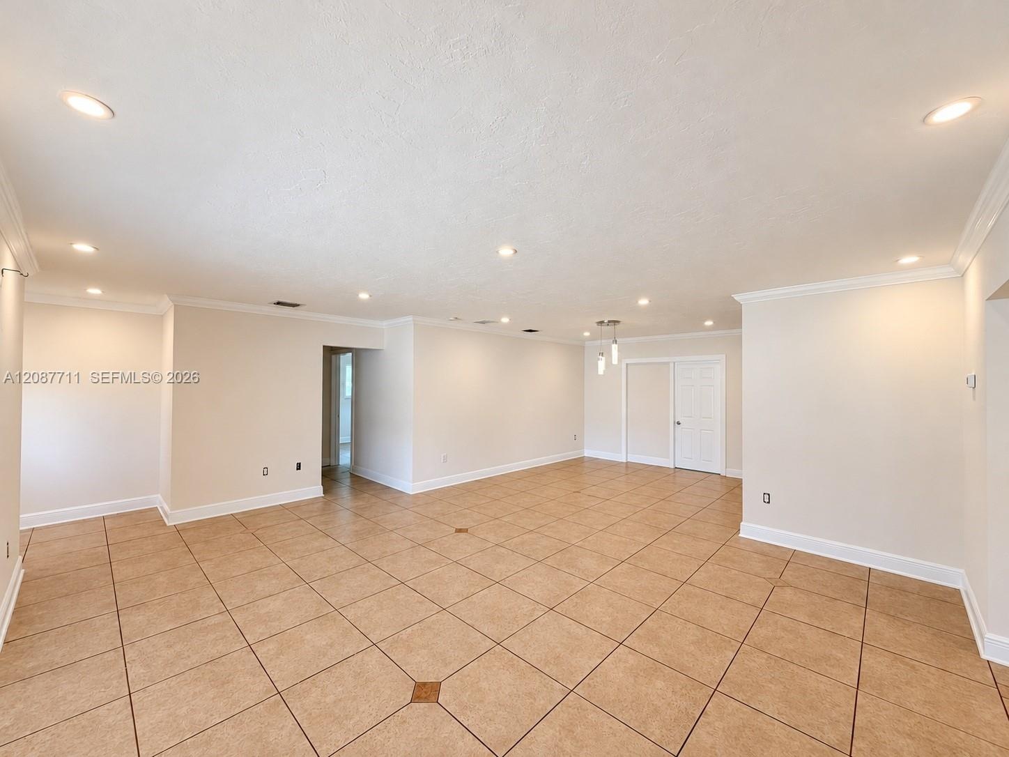 Open-concept room featuring large-format ceramic tile flooring with decorative inserts, recessed lighting, crown molding, and a multi-pendant light fi