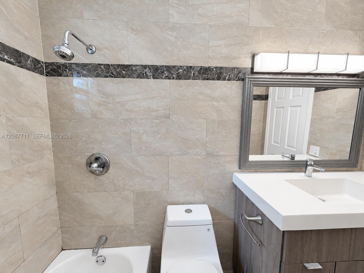 Bathroom featuring floor-to-ceiling tile with a contrasting decorative inlay, a wood-finish vanity with a white countertop and integrated sink, a cont