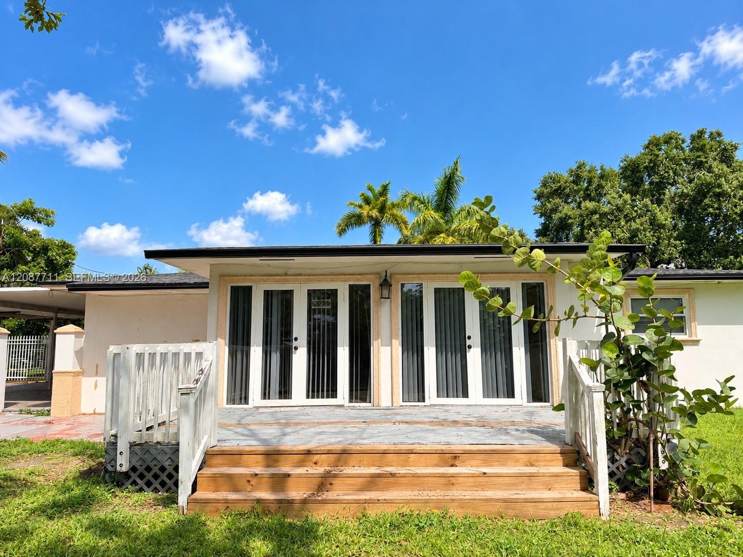 Exterior deck featuring wood stairs, white railing, dual sets of glass-paned doors, and a covered patio area