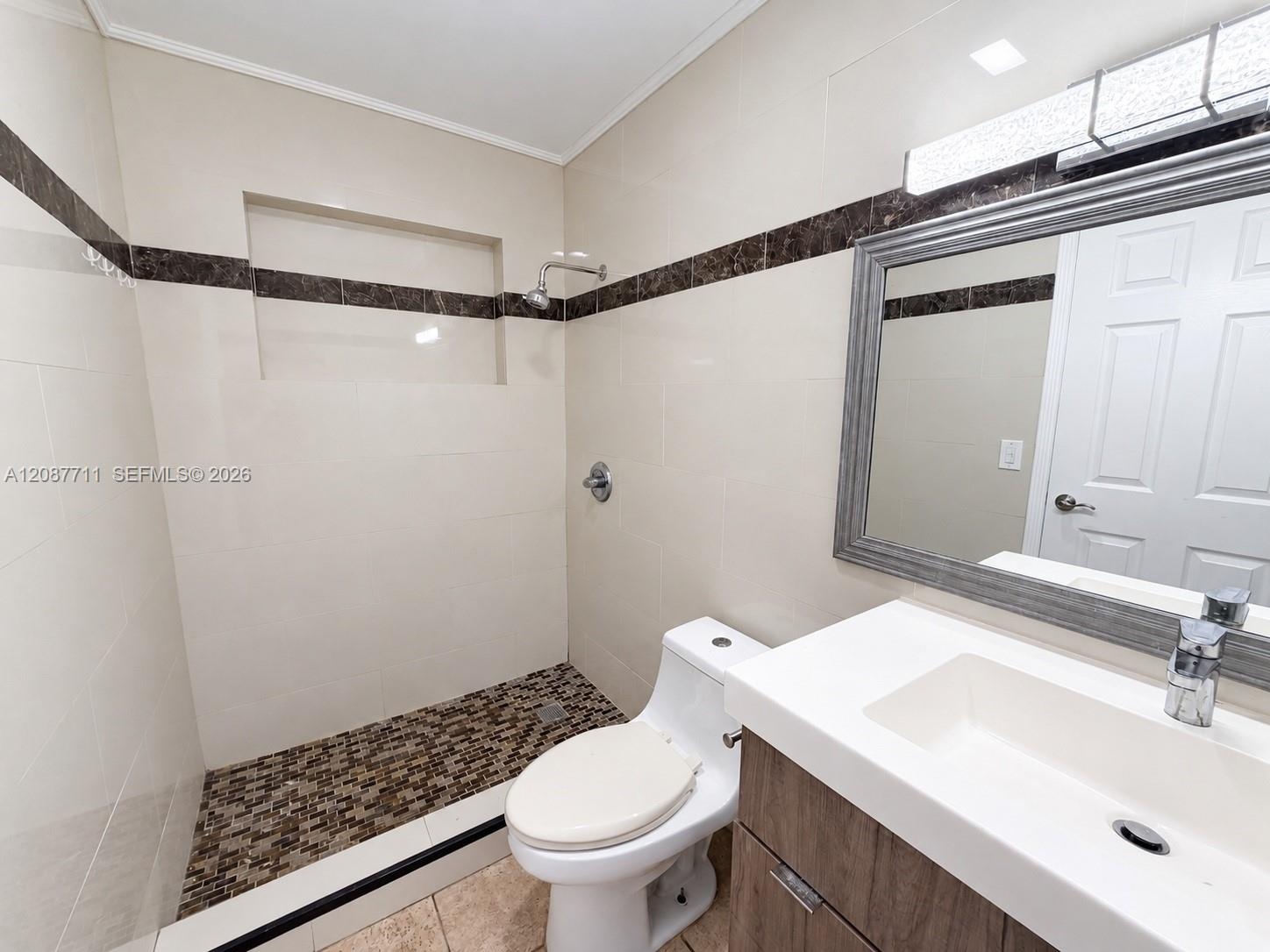 Bathroom featuring large-format wall tile with decorative stone inlay, a walk-in shower with stone mosaic flooring and built-in recessed shelving, and