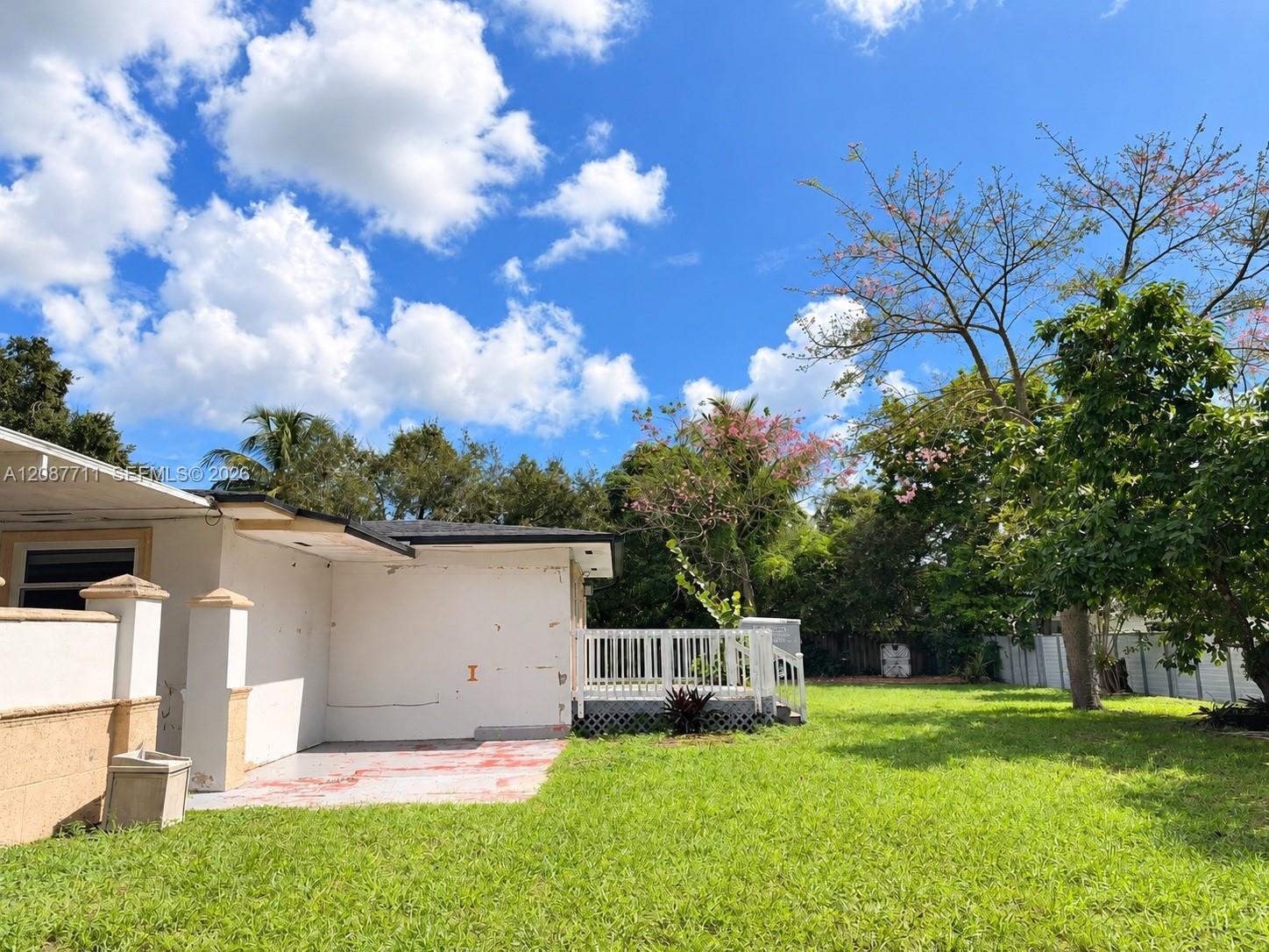 Expansive backyard featuring a manicured lawn, white wood-slat deck, masonry perimeter fencing, and mature trees