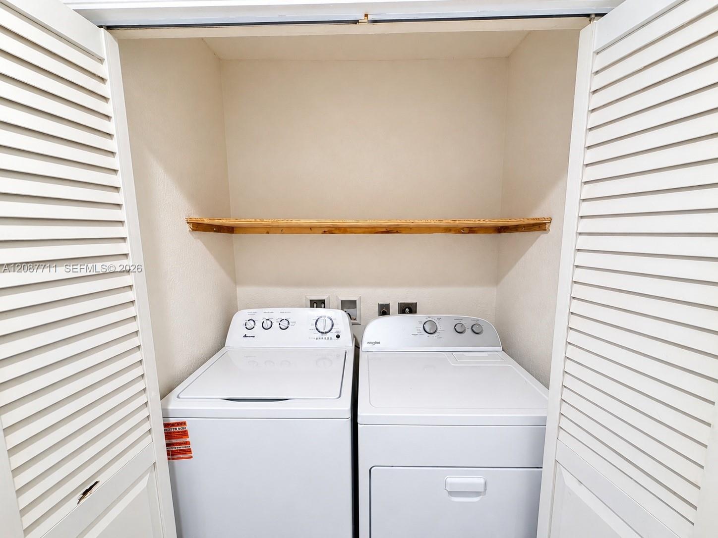 Laundry closet featuring white louvered doors and an installed wooden shelf