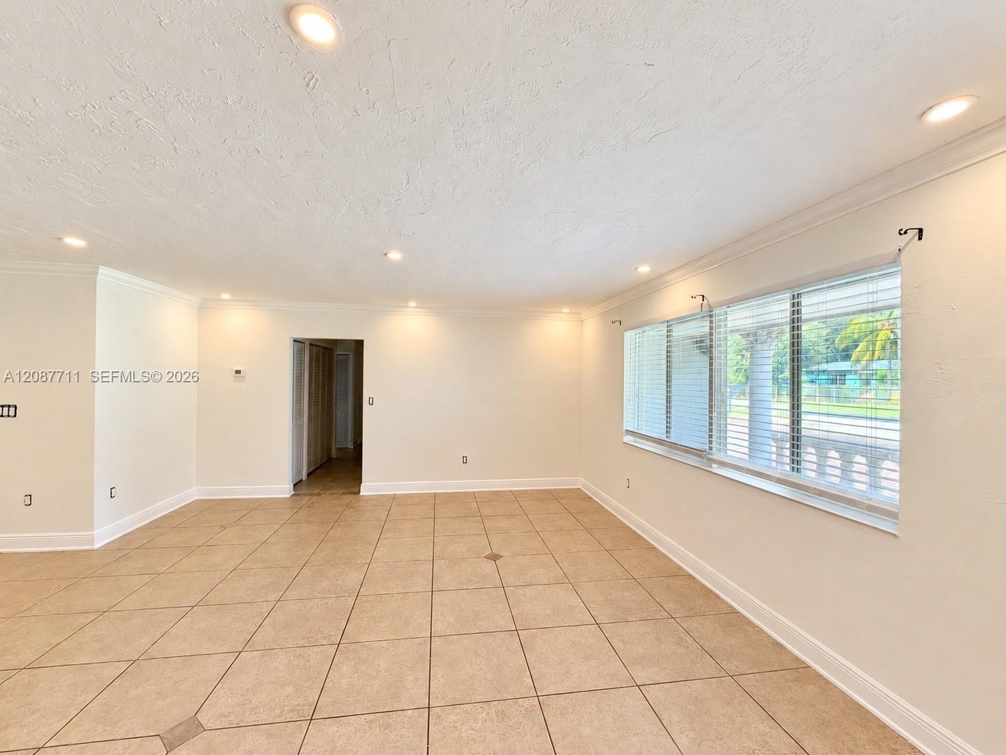 Neutral-toned tile flooring, recessed lighting, expansive multi-pane window with horizontal blinds, and crown molding