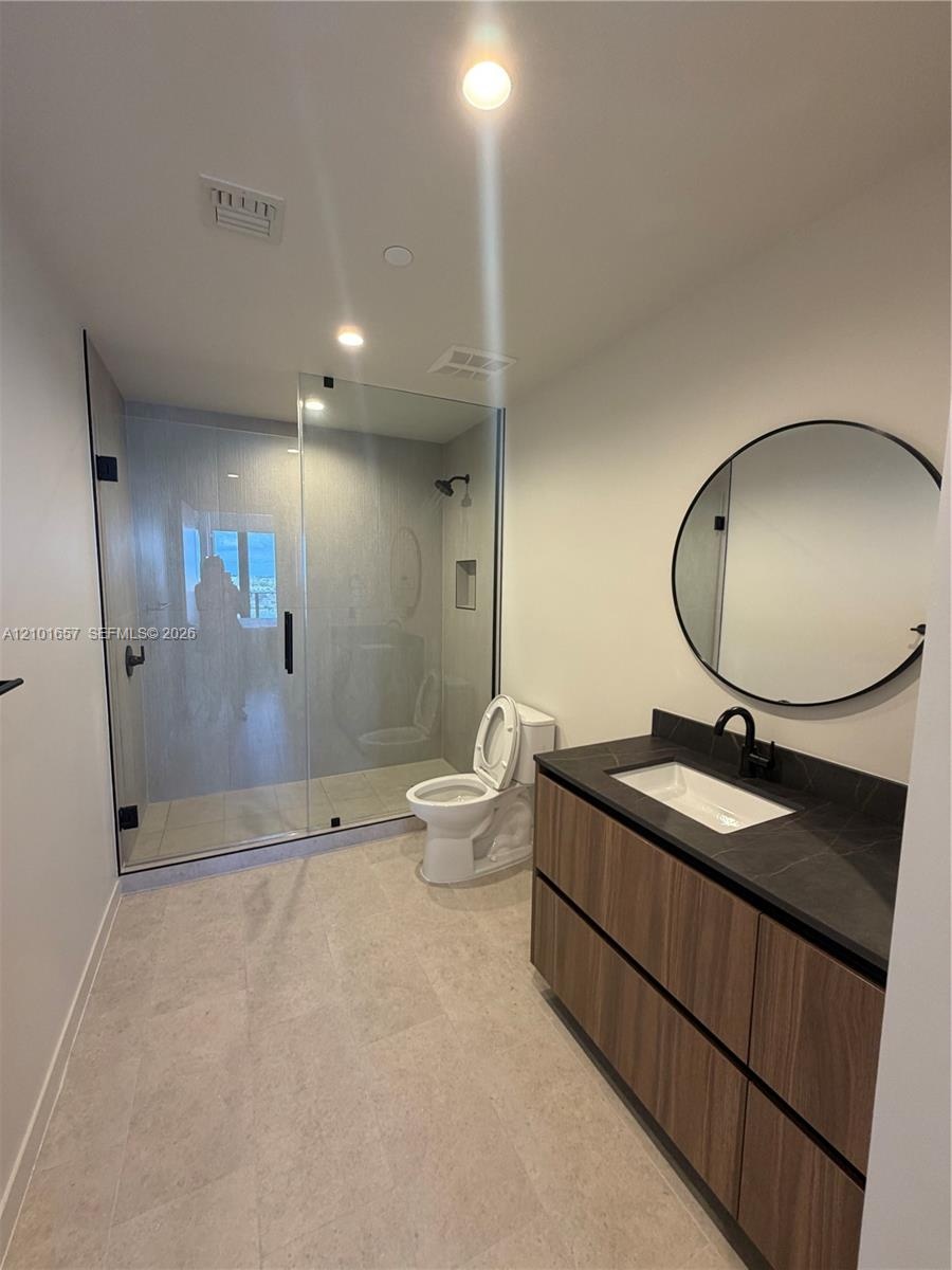 Floating vanity featuring wood-finish cabinetry, dark countertop, and integrated rectangular sink, paired with a frameless glass-enclosed shower, matt