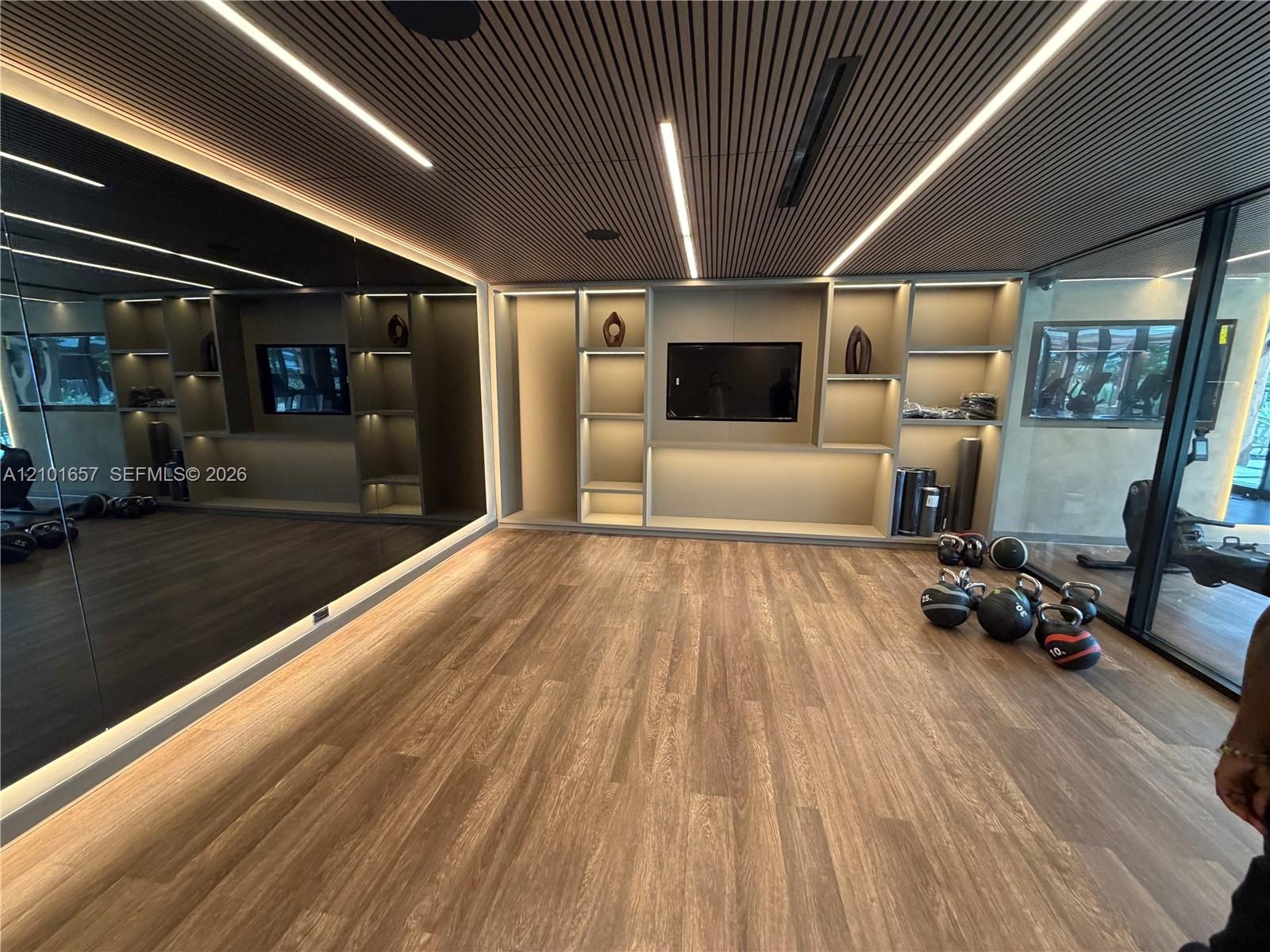 Slatted wood ceiling with recessed linear lighting, full-height wall mirror, wood-finish flooring, and built-in display shelving featuring integrated 