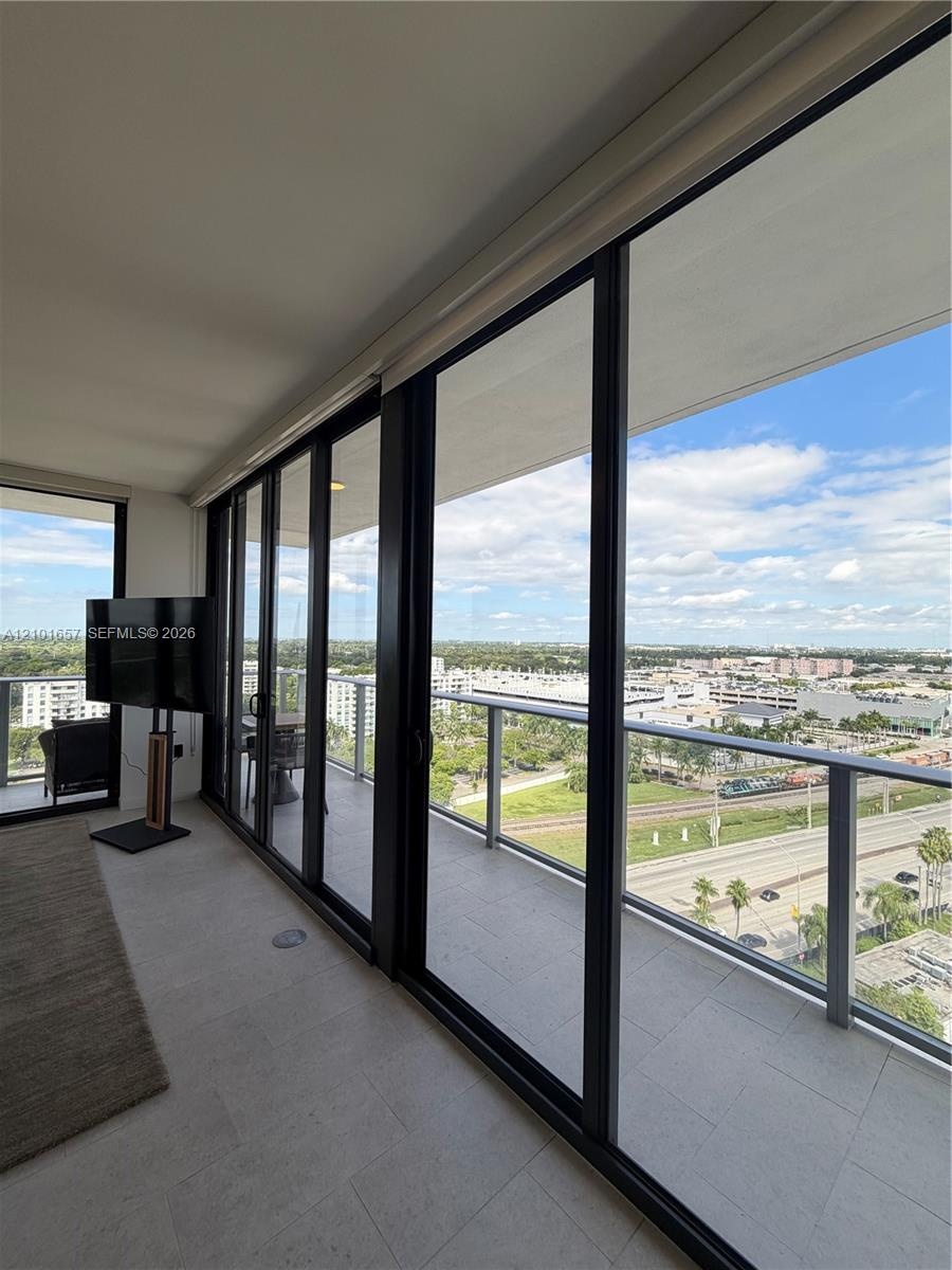 Floor-to-ceiling glass sliding doors, covered exterior balcony, stone-finish flooring, and metal railing