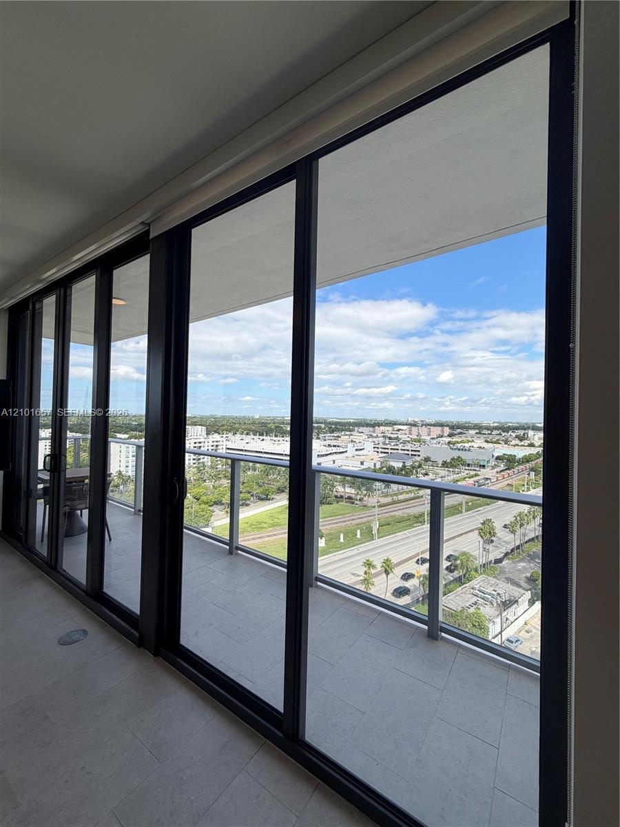 Floor-to-ceiling sliding glass panels, covered balcony with tile flooring, and metal-railing enclosure