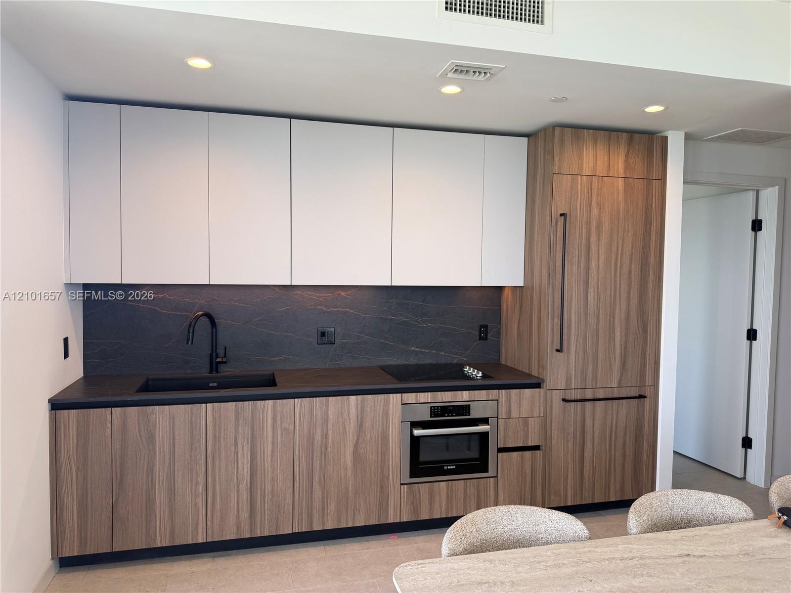 Modern kitchen featuring two-tone cabinetry with wood-finish lower cabinets, matte white upper cabinets, integrated refrigerator, stone backsplash, an