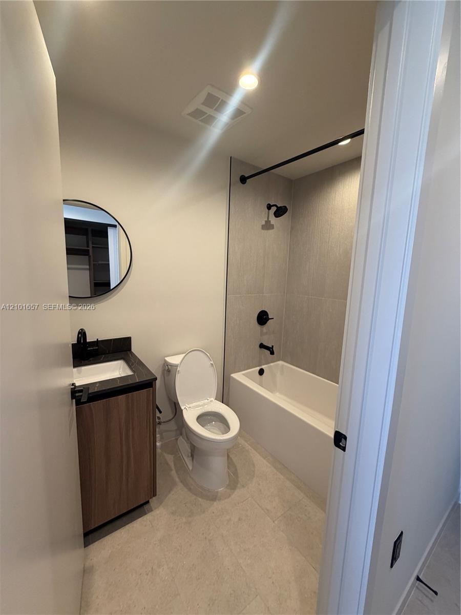 Bathroom featuring a wood-finish vanity with a dark stone countertop, circular mirror, and matte black hardware including a shower-tub faucet assembly