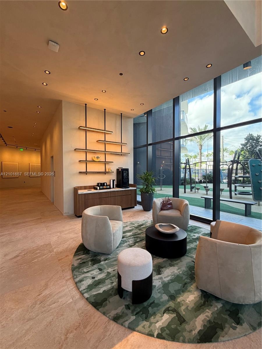 Floor-to-ceiling glass windows, recessed ceiling lighting, natural stone flooring, custom wall-mounted metal shelving, and a built-in wood-finish cred