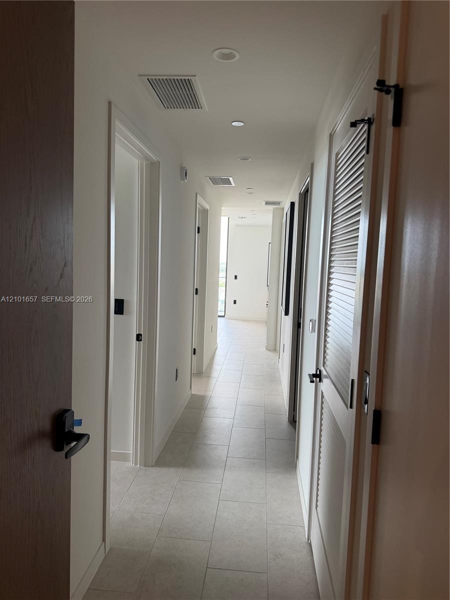 Hallway featuring large-format ceramic tile flooring, recessed ceiling lighting, and matte black hardware on solid-core wood doors, including a louver