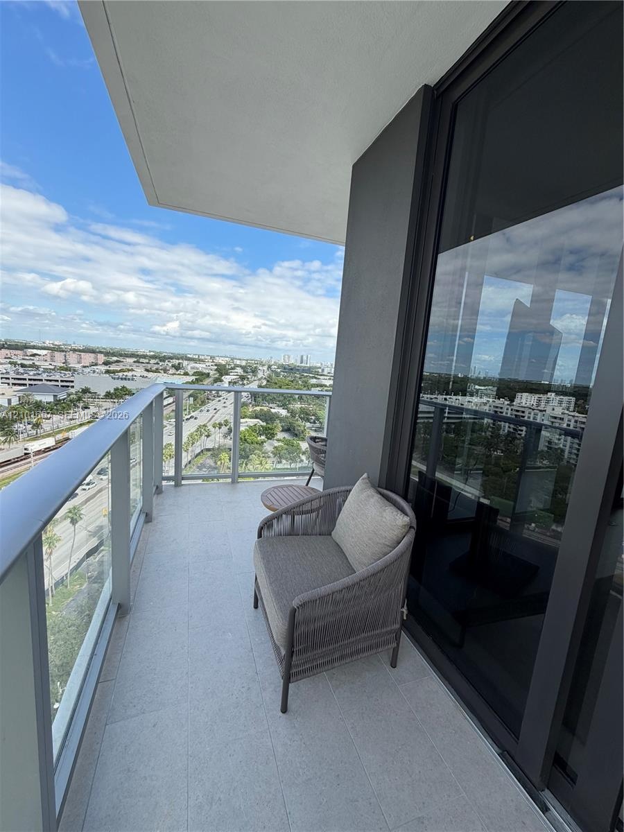 Covered balcony featuring concrete flooring, a glass panel railing, and expansive sliding glass doors