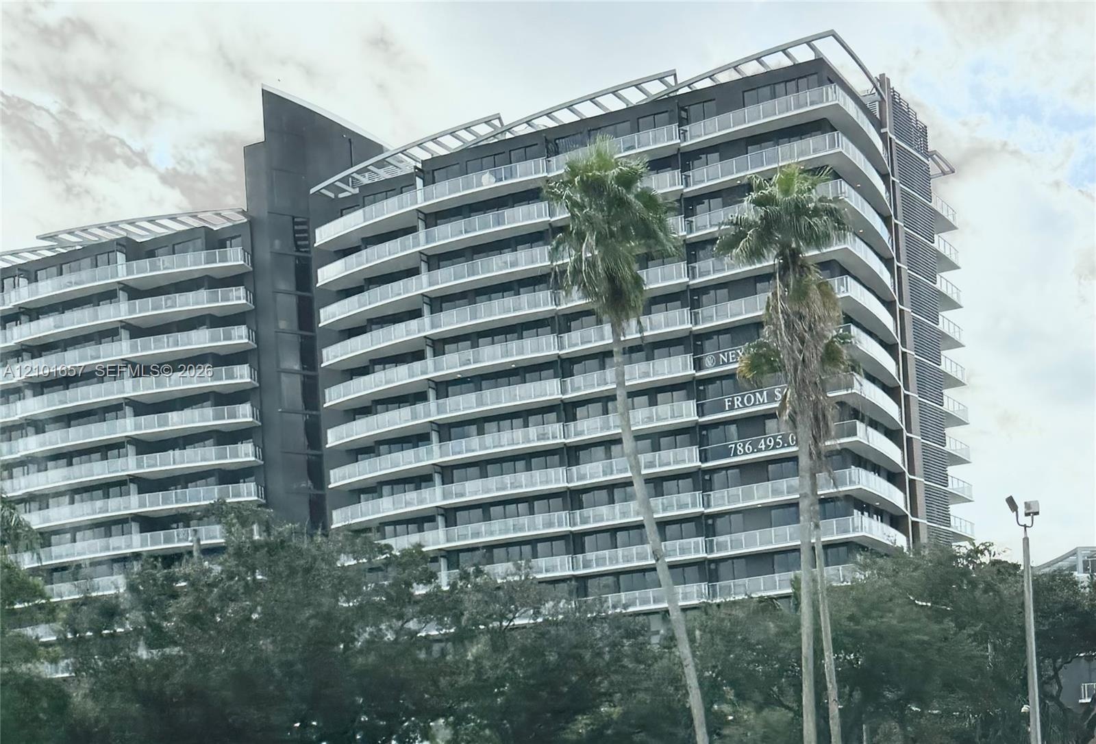 Modern high-rise exterior featuring a dark metallic facade, rhythmic rows of glass-railed balconies, and a stepped roofline