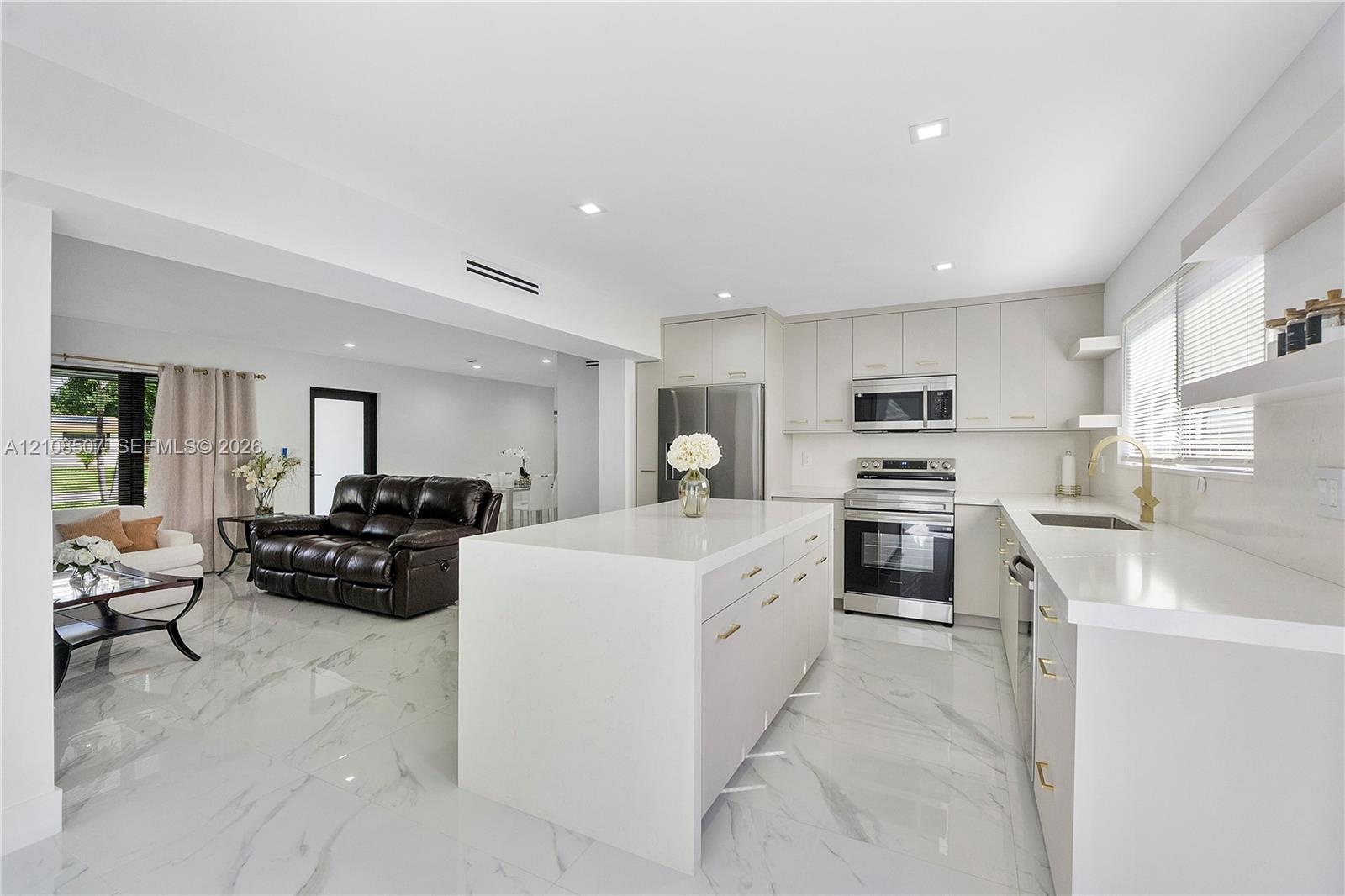 Kitchen featuring a central island with a solid-surface countertop, flat-panel cabinetry, stainless steel appliances, and large-format porcelain tile 