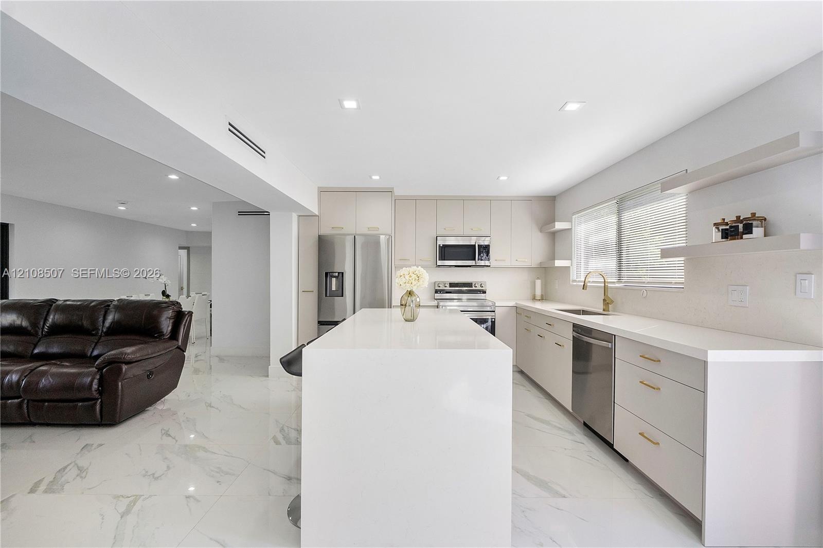 Kitchen featuring a stone-finish waterfall island, flat-panel cabinetry, stainless steel appliances, floating wall shelving, and large-format tile flo