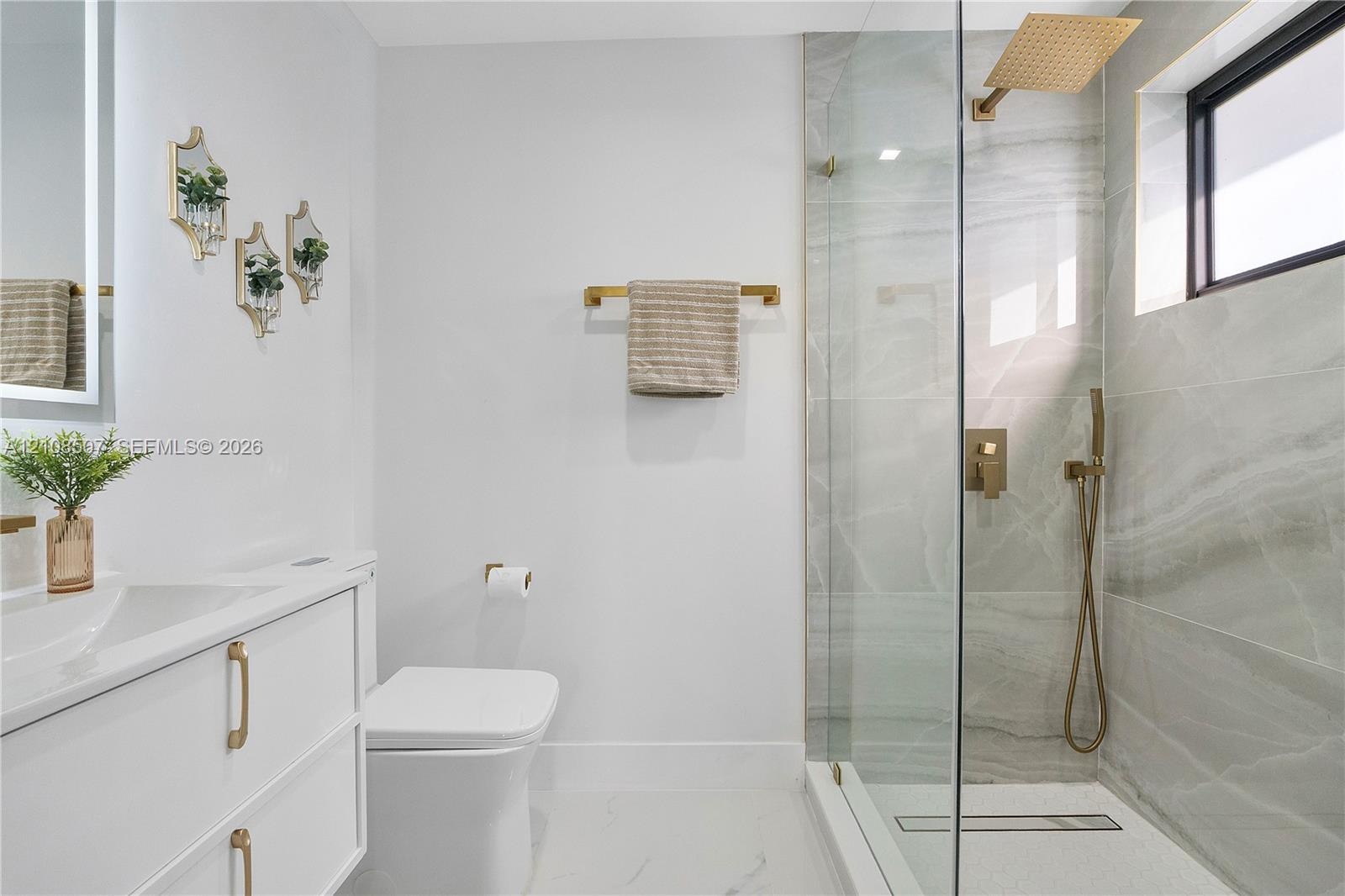Bathroom featuring a white vanity with gold-tone hardware, large-format tiled walk-in shower with a rain-style showerhead, and matching gold-tone fixt