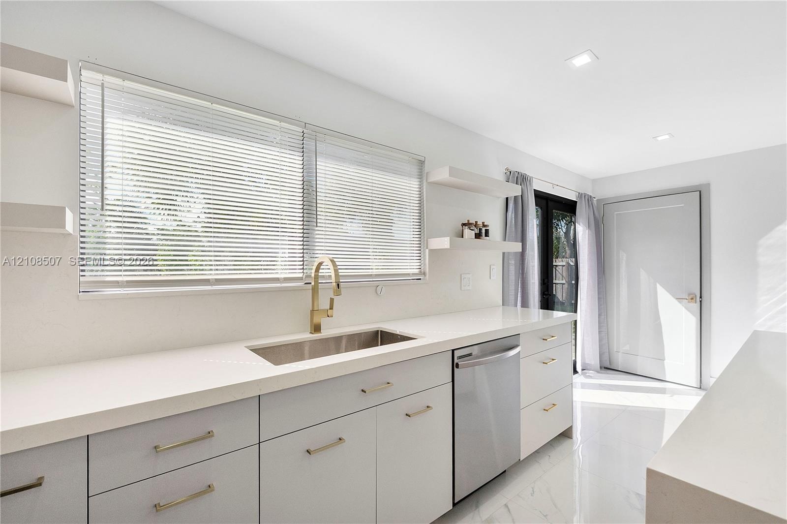 Kitchen featuring light-toned cabinetry, solid surface countertops, a stainless steel undermount sink with a brass-finish faucet, built-in stainless s