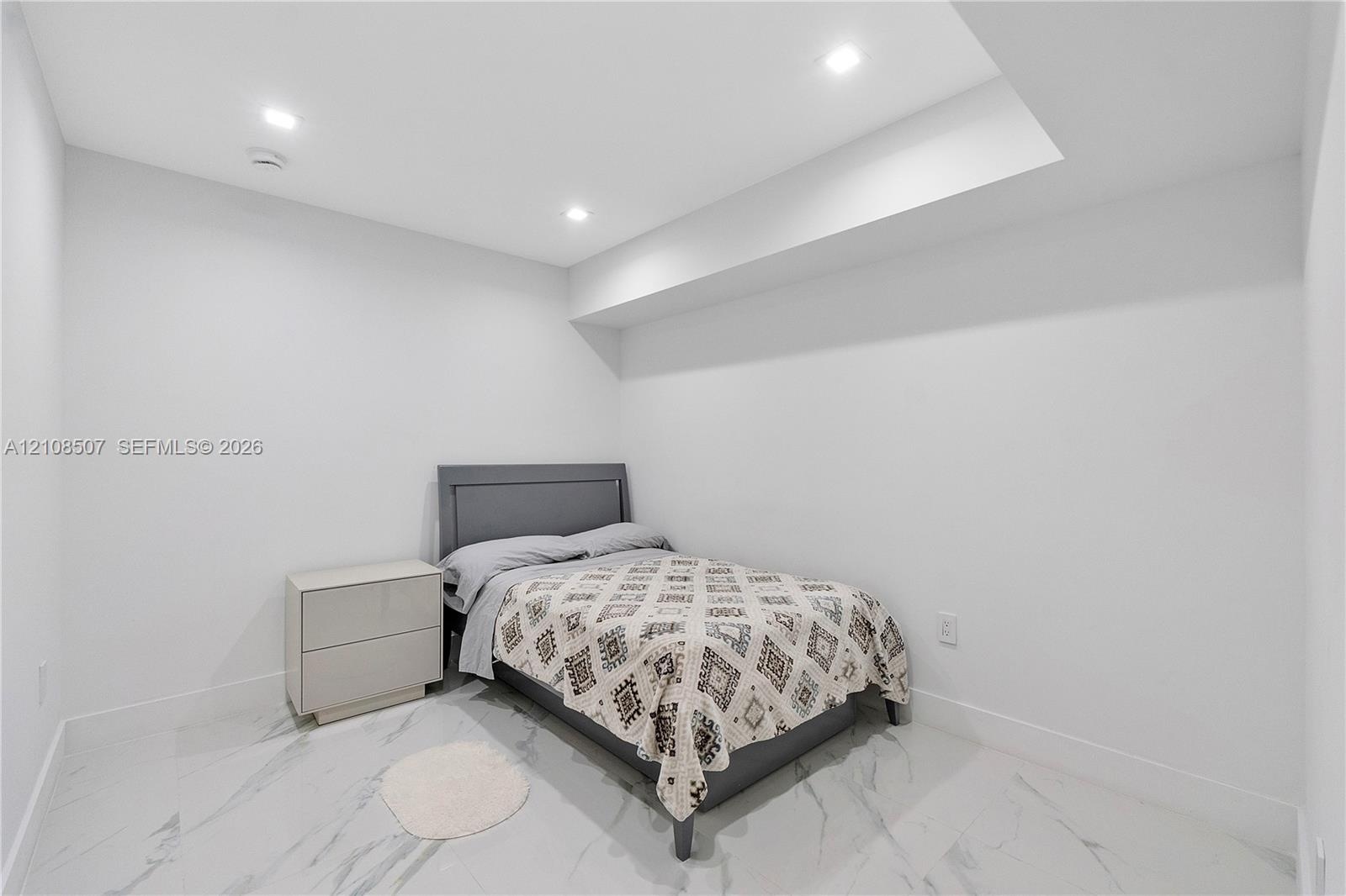 Neutral-toned interior space featuring light-colored stone-finish tile flooring, recessed ceiling lighting, and a recessed ceiling architectural detai