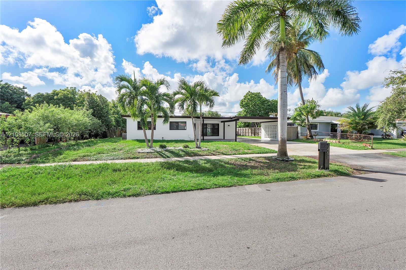 Single-story residence featuring a white stucco exterior, attached carport with decorative breeze block screen, concrete driveway, and mature palm tre