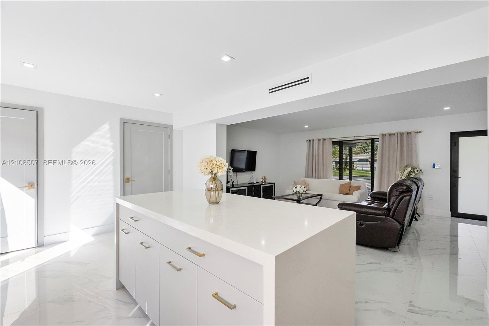 Center island featuring a white stone-surface countertop, recessed ceiling lighting, light-toned cabinetry with metallic hardware, and white tile floo