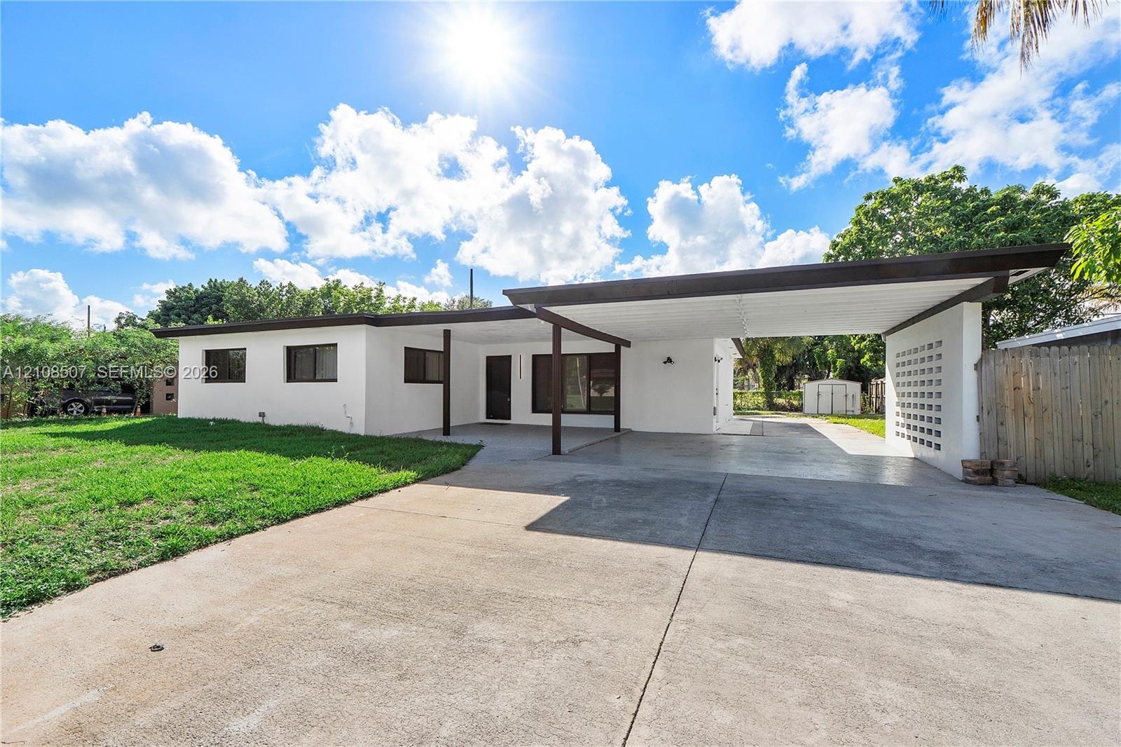 Single-story residence featuring a smooth stucco exterior, attached flat-roof carport, decorative concrete block screening, and an expansive concrete 
