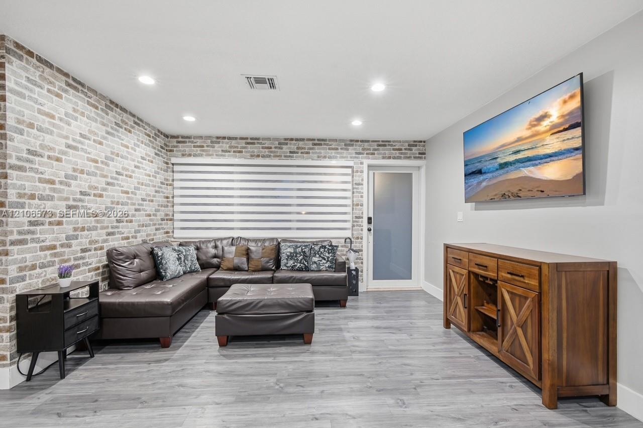 Living space featuring a brick accent wall, wood-finish flooring, recessed lighting, and a frosted glass door