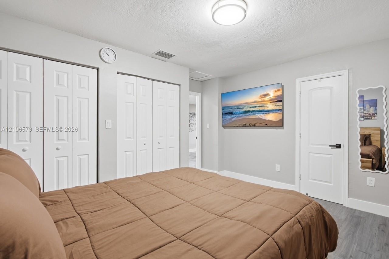 Room featuring wood-finish flooring, two sets of bifold closet doors, a solid-core interior door with matte black hardware, and a flush-mount ceiling 