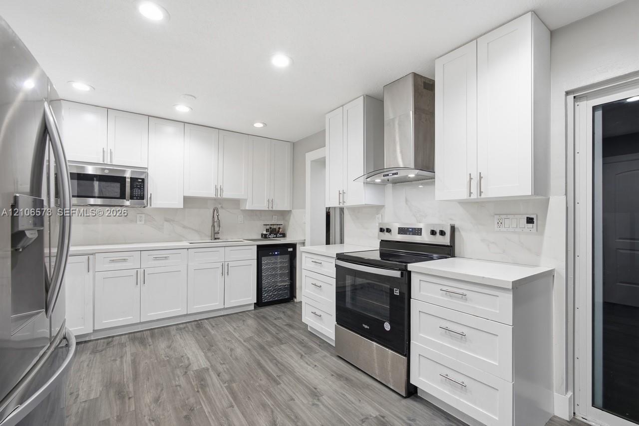 Kitchen featuring white Shaker-style cabinetry, quartz countertops, stainless steel appliances, a built-in wine refrigerator, and wood-finish flooring