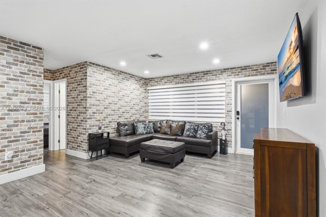 Interior featuring brick veneer accent walls, wood-finish flooring, recessed lighting, and a frosted glass exterior door
