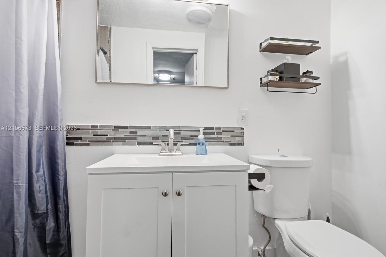 Bathroom featuring a white vanity cabinet with a integrated sink, metallic faucet, rectangular wall-mounted mirror, decorative horizontal mosaic tile 