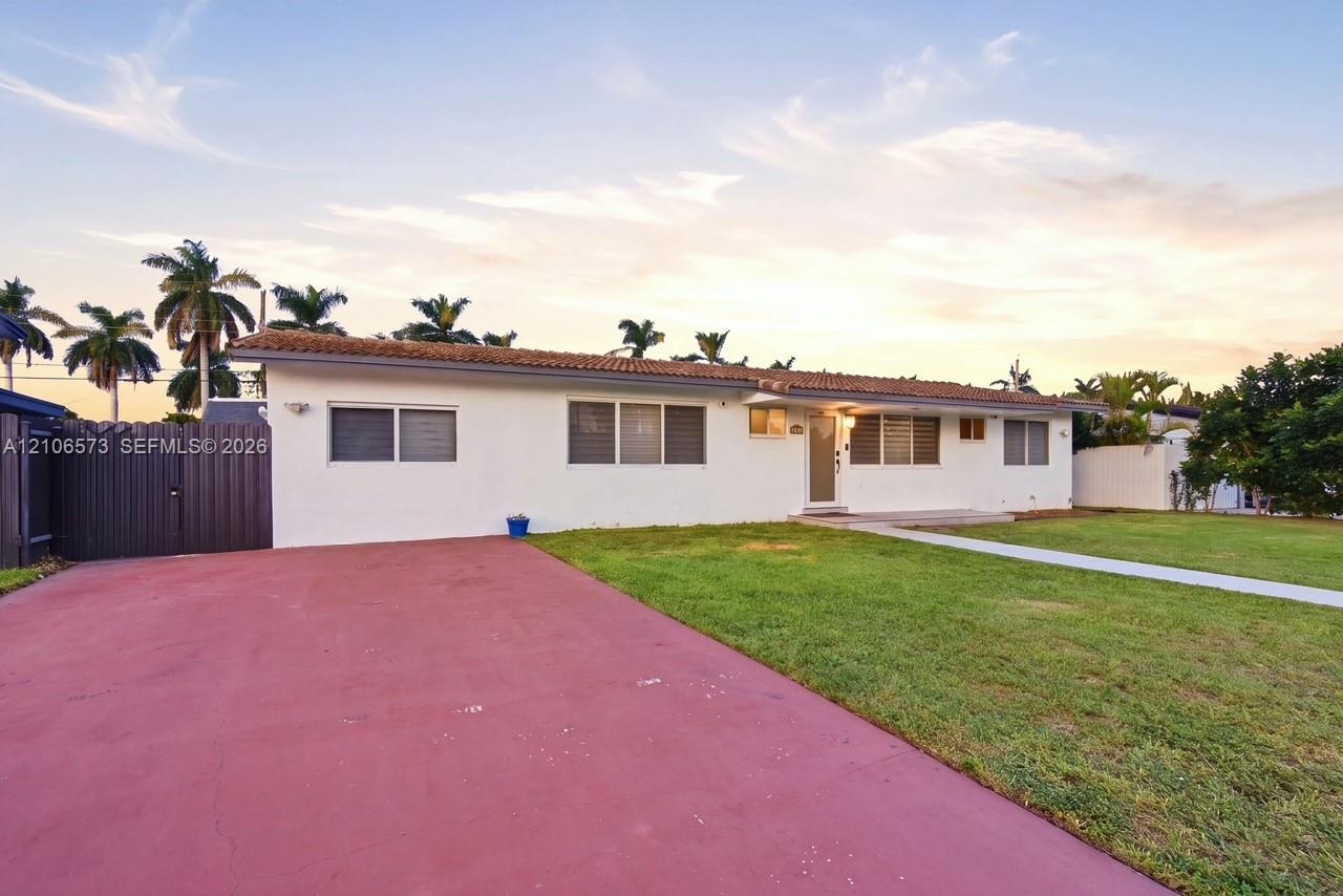 Single-story residence featuring a tile roof, light-colored exterior finish, expansive paved driveway, and manicured lawn