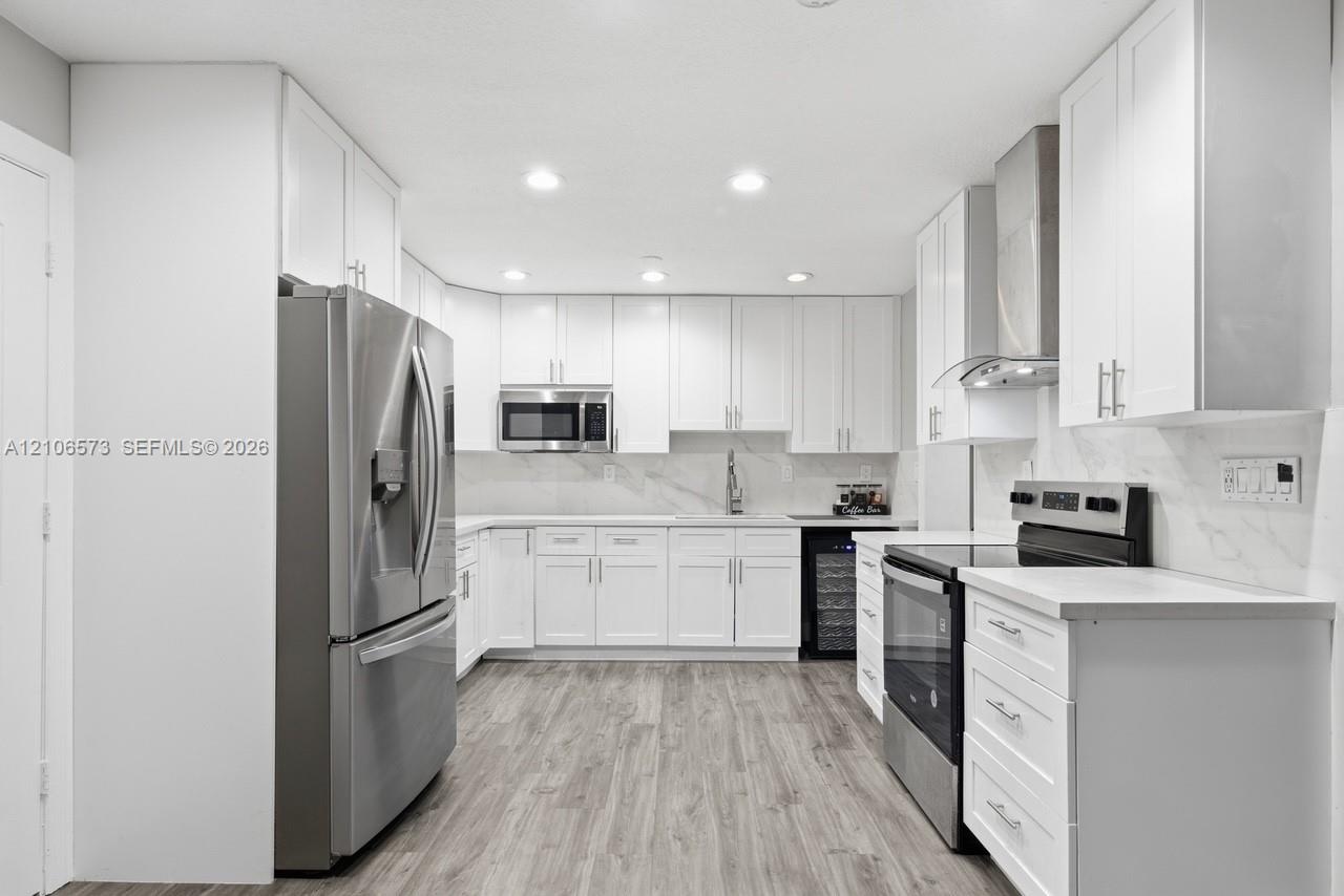Kitchen featuring white shaker-style cabinetry, stainless steel appliances, stone-look backsplash, wood-finish flooring, and recessed ceiling lighting