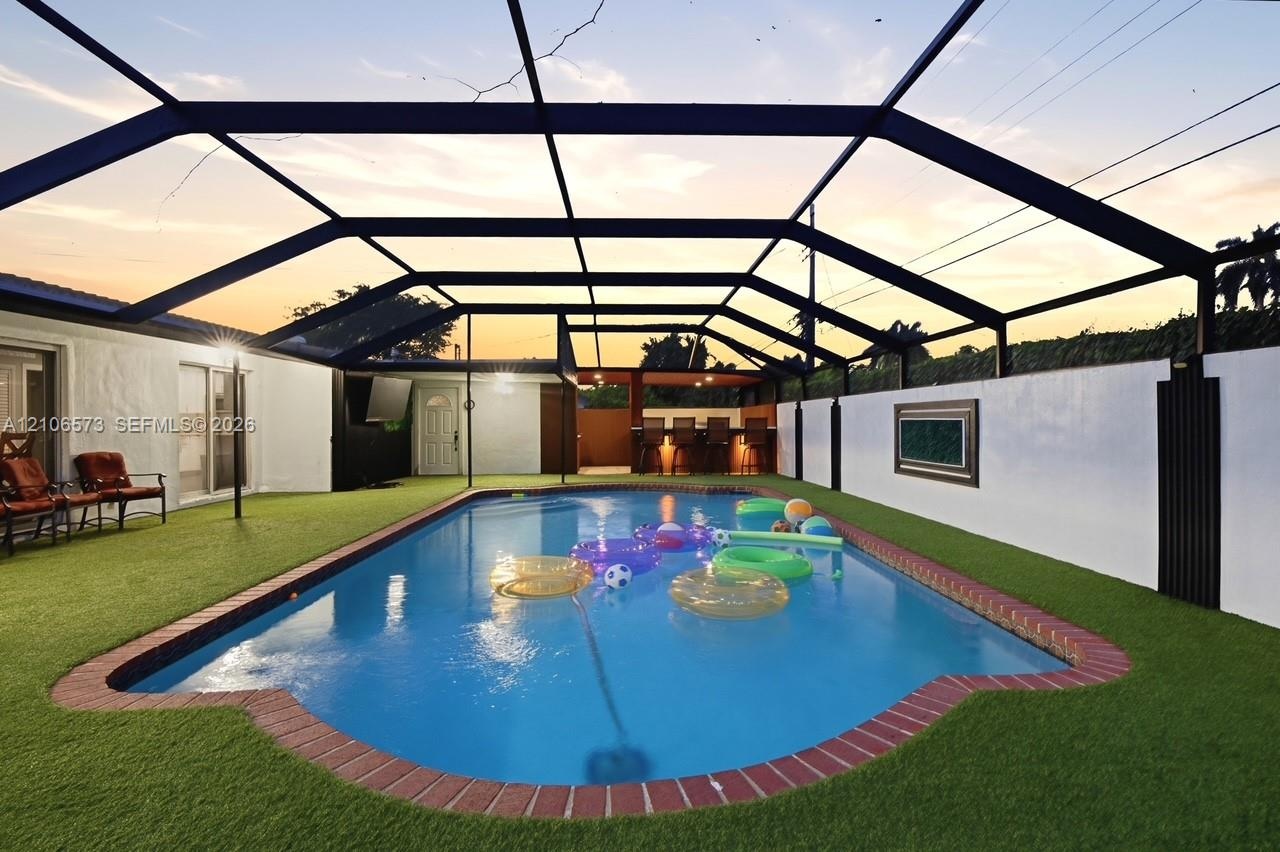 Screened-in pool area featuring brick coping, synthetic turf surfacing, and a built-in outdoor wet bar