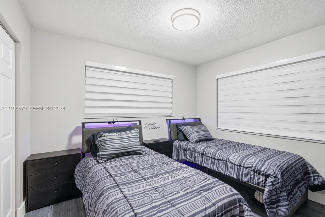 Neutral wall palette with wood-finish flooring, dual windows equipped with horizontal roller shades, and a flush-mount circular ceiling light fixture