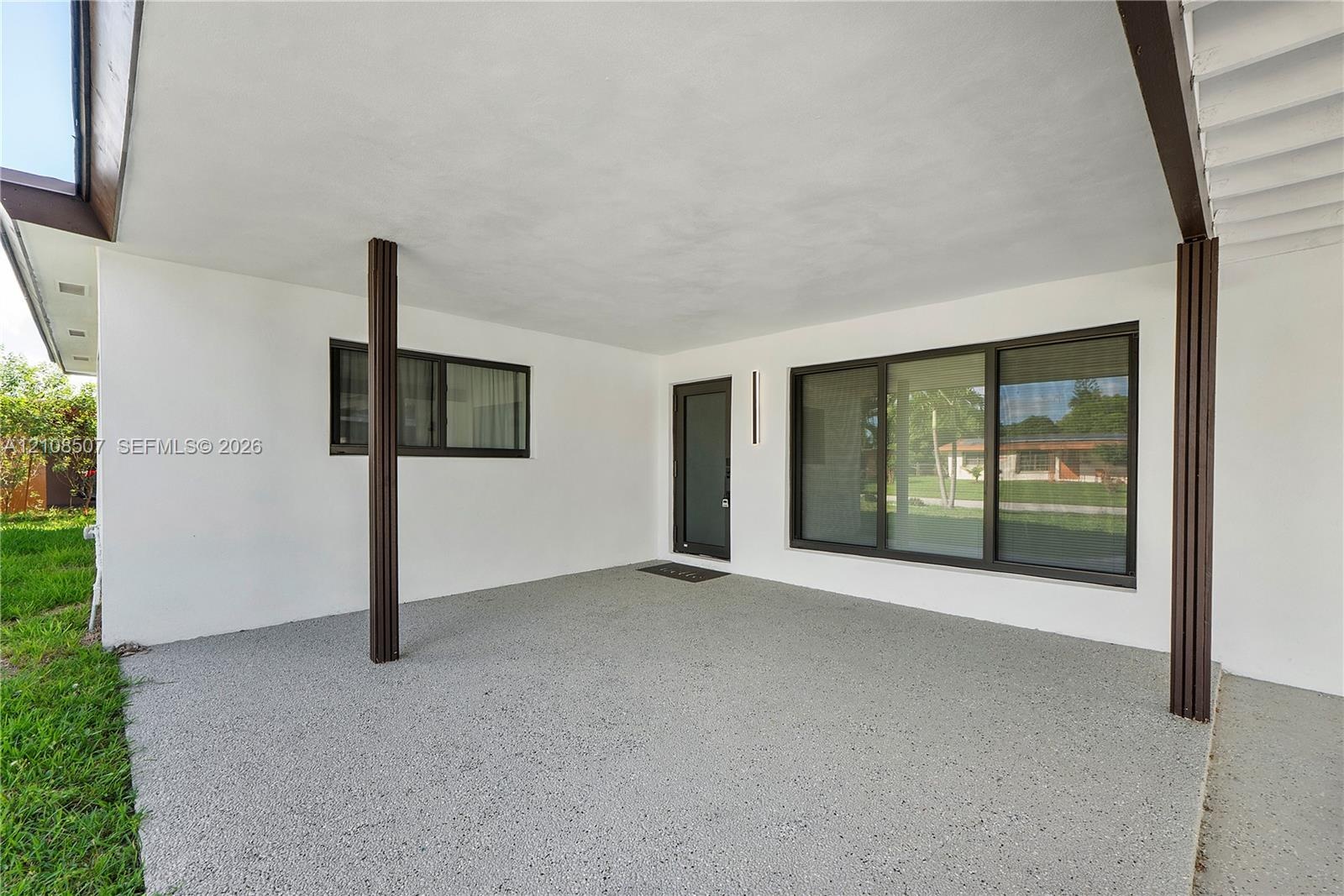 Covered patio featuring an aggregate concrete floor, dark-finished structural support columns, a glass-panel entry door, and large-format multi-pane w