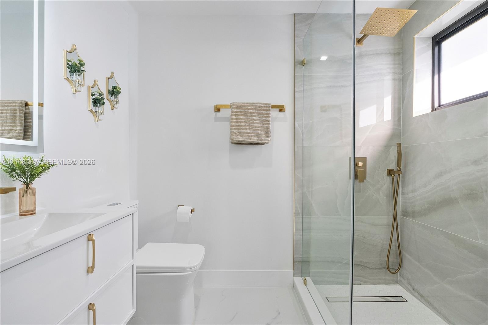 Floating vanity with integrated sink, brass hardware, walk-in shower with glass enclosure, wall-mounted rainfall showerhead, and tile-surround shower 