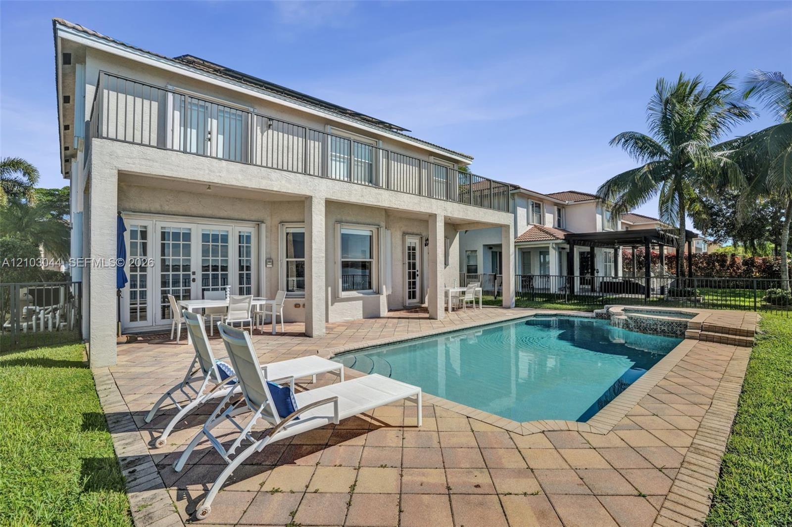 Stucco exterior featuring a second-story balcony with metal railings, a covered ground-level patio, and a concrete-paver pool deck surrounding an ingr